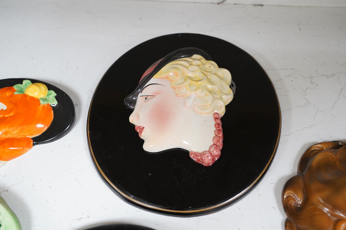 Six Art Deco style composition and pottery wall masks, largest 30cm high. Condition - fair, one mask detached from plaque